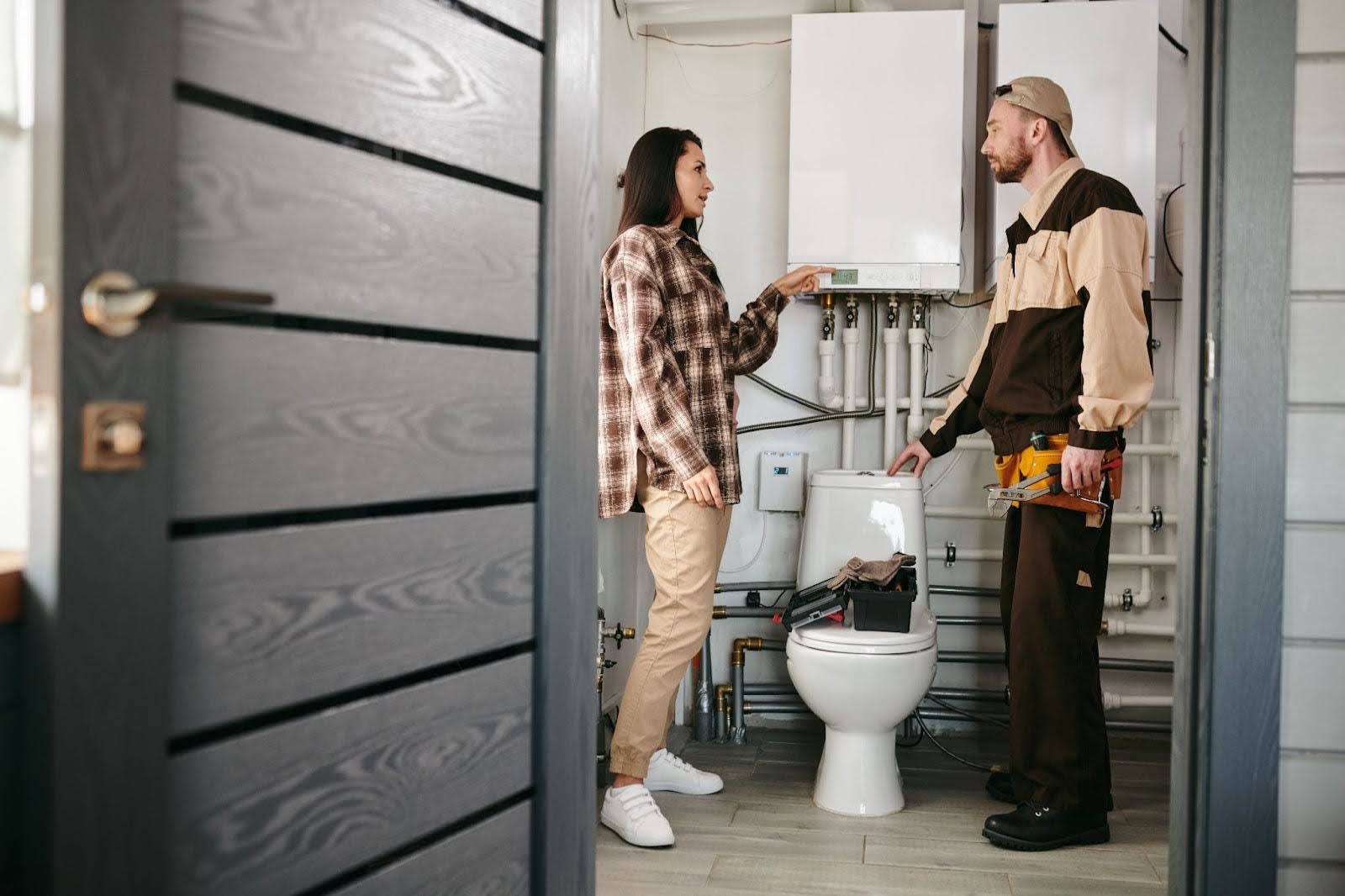 Plumber speaking to a woman and inspecting a toilet and pipes.