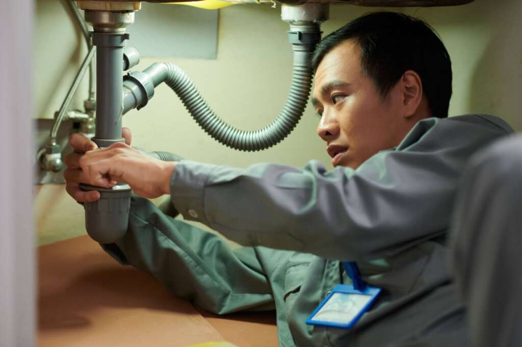 Plumber under a sink working with a pipe.