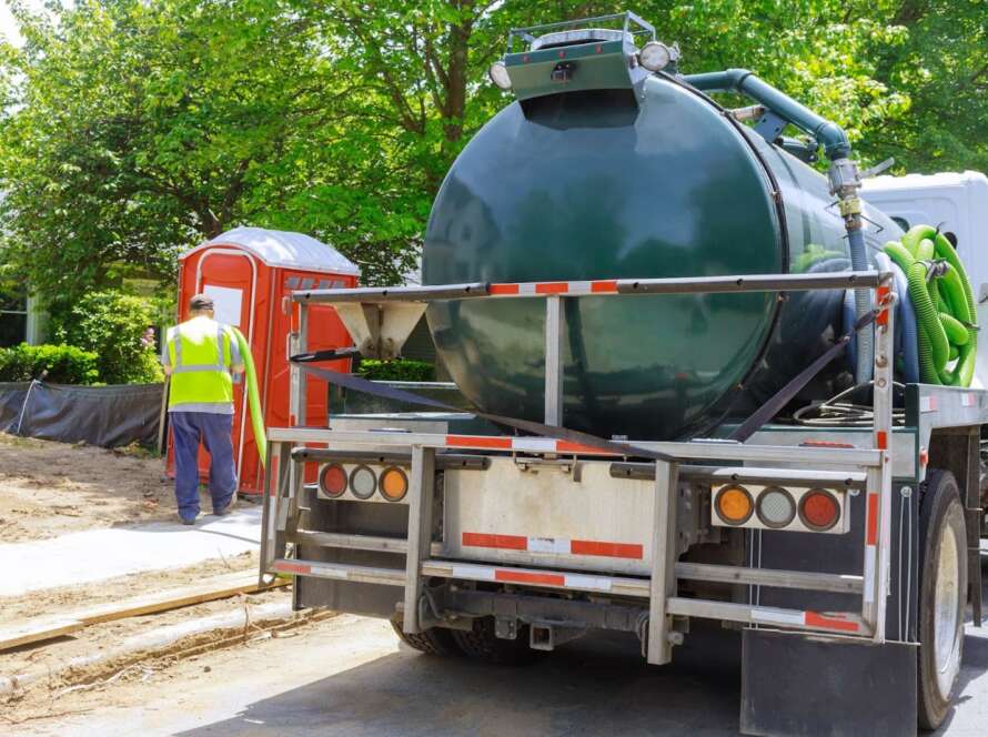 A worker using a sewage truck for septic tank pumping, removing waste from a rental toilet for proper disposal and cleaning.