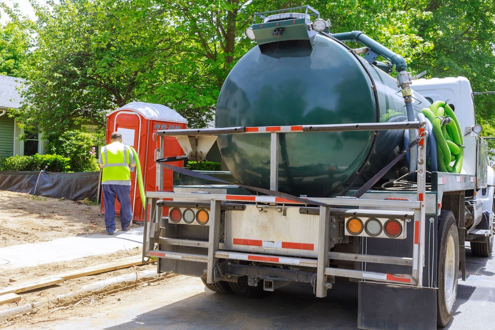 A worker using a sewage truck for septic tank pumping, removing waste from a rental toilet for proper disposal and cleaning.