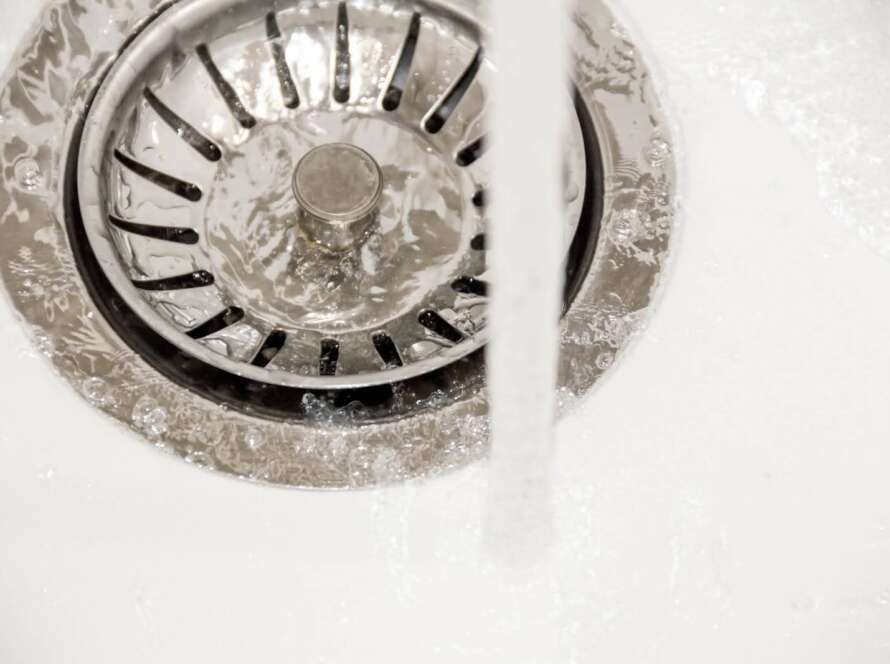 A close-up of water flowing from the faucet into a sink's drainage.