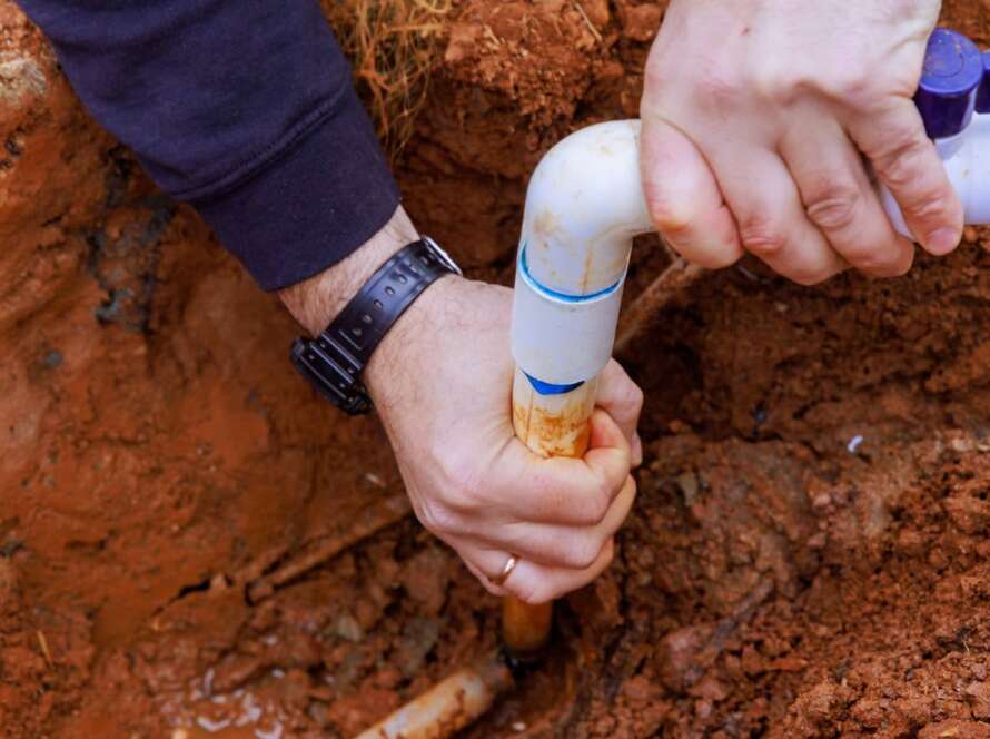 Close-up of a plumber applying PVC glue to connect replacement pipes in a home sewer line system.