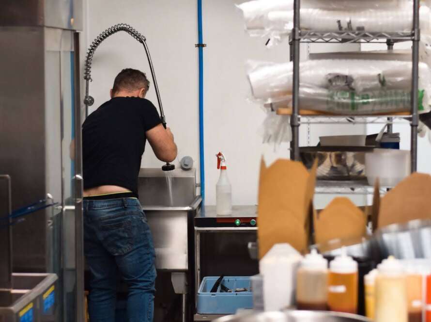 Rear view of a restaurant crew washing dishes in a large industrial sink.