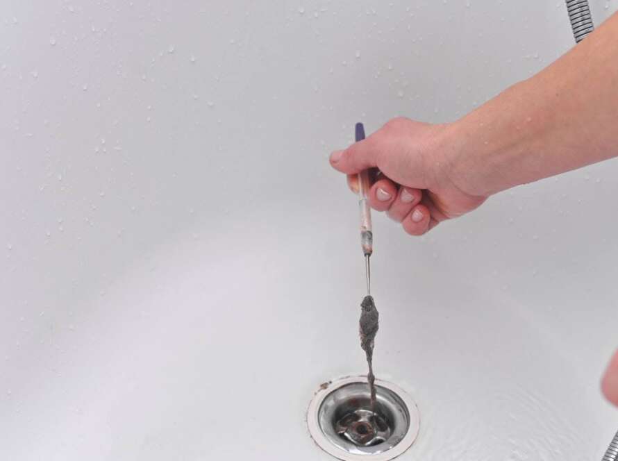 A man’s hand cleans a bathtub drain to remove clogs and debris, restoring smooth water flow.