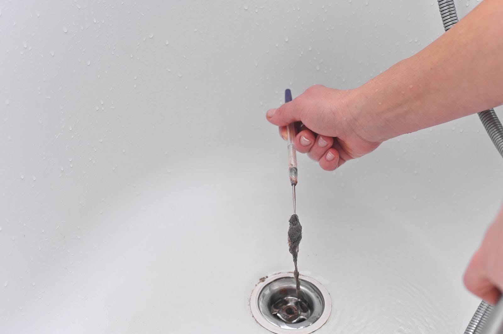 A man’s hand cleans a bathtub drain to remove clogs and debris, restoring smooth water flow.
