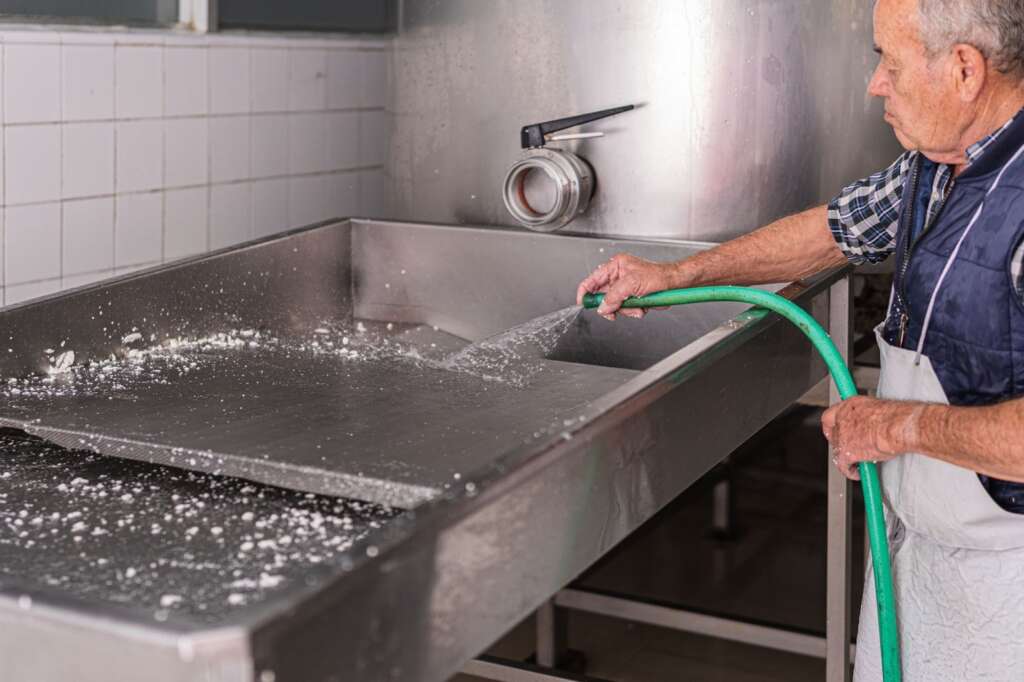 Senior employee cleaning the production floor of a cheese factory with a water hose.