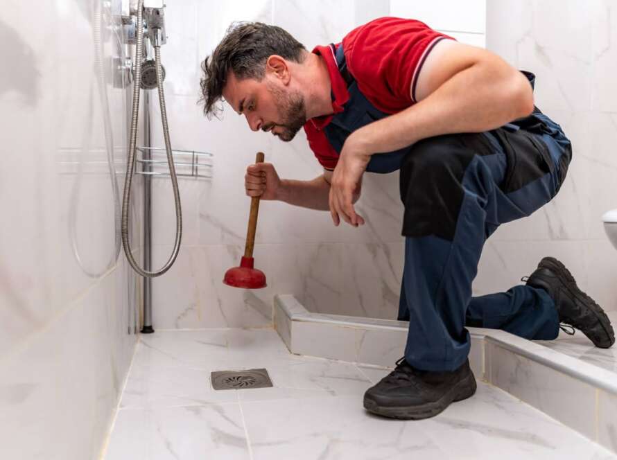 A plumber plunging a shower drain as part of troubleshooting a clogged sewer line issue.