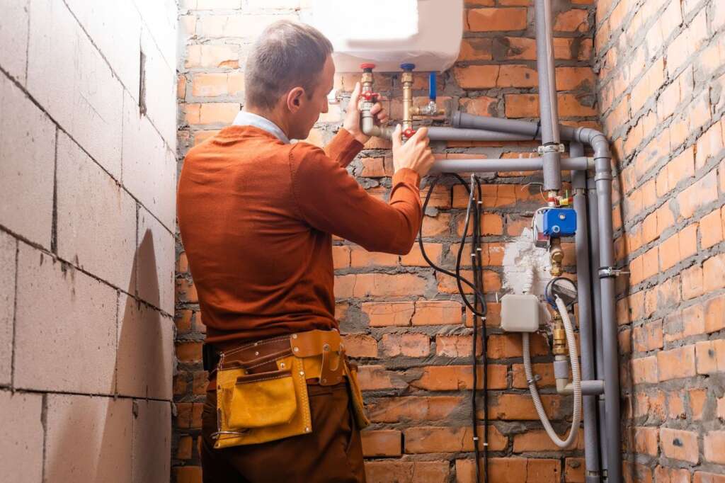 Plumber performing a leak inspection on basement pipes in a residential home.