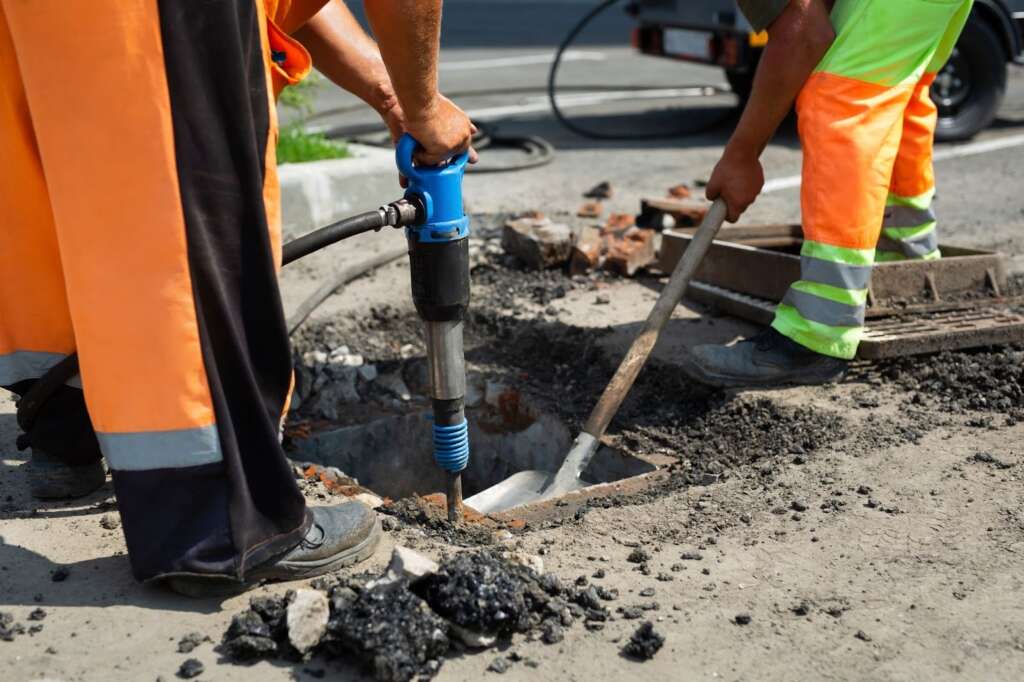 Workers dig through asphalt to get to a broken sewer line.