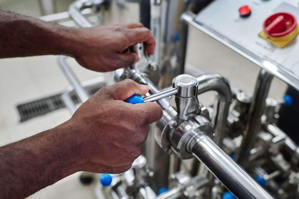 Close-up of a plumber’s hands adjusting pipe valves while addressing a plumbing problem in a commercial facility.