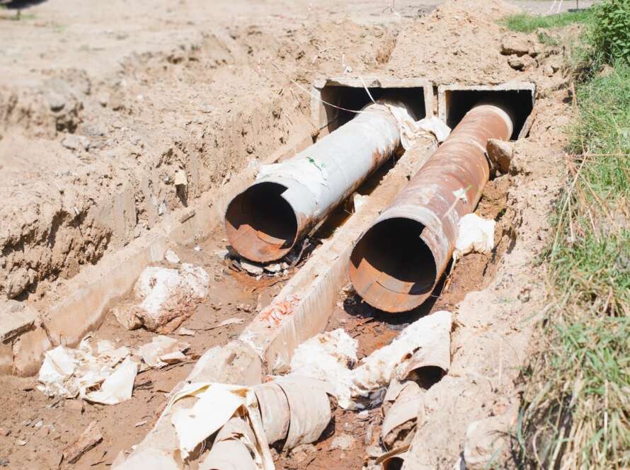 Plumbing repair showing old, rusty sewer pipes exposed in an outdoor dug hole during replacement work.