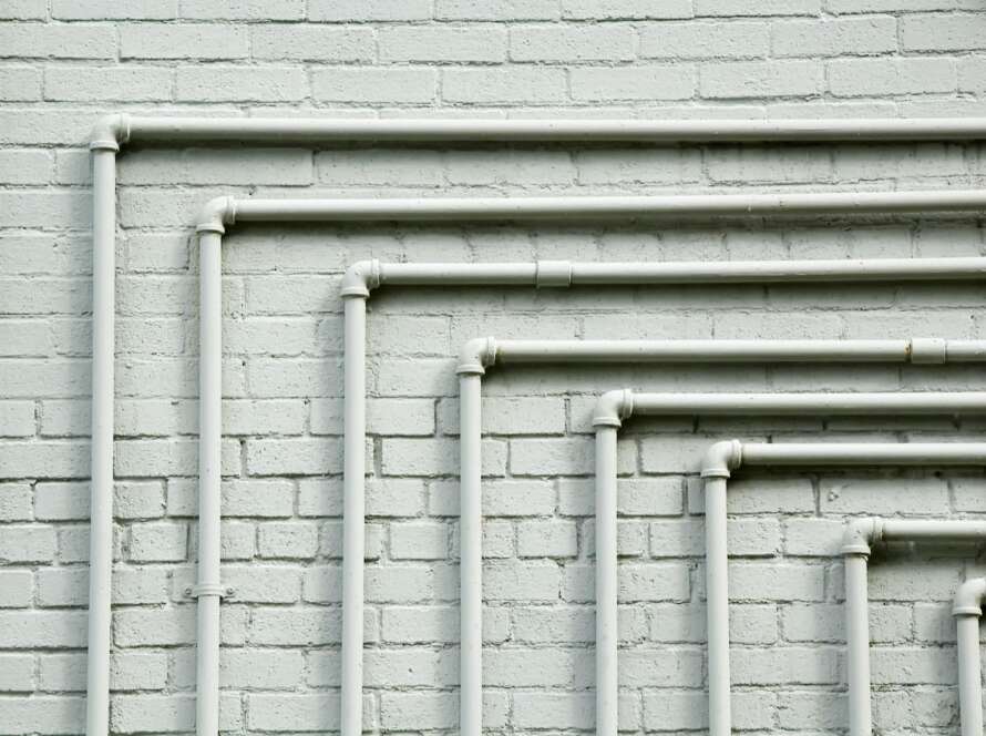 Parallel drain pipes featuring 90-degree turns mounted against a whitewashed brick wall.