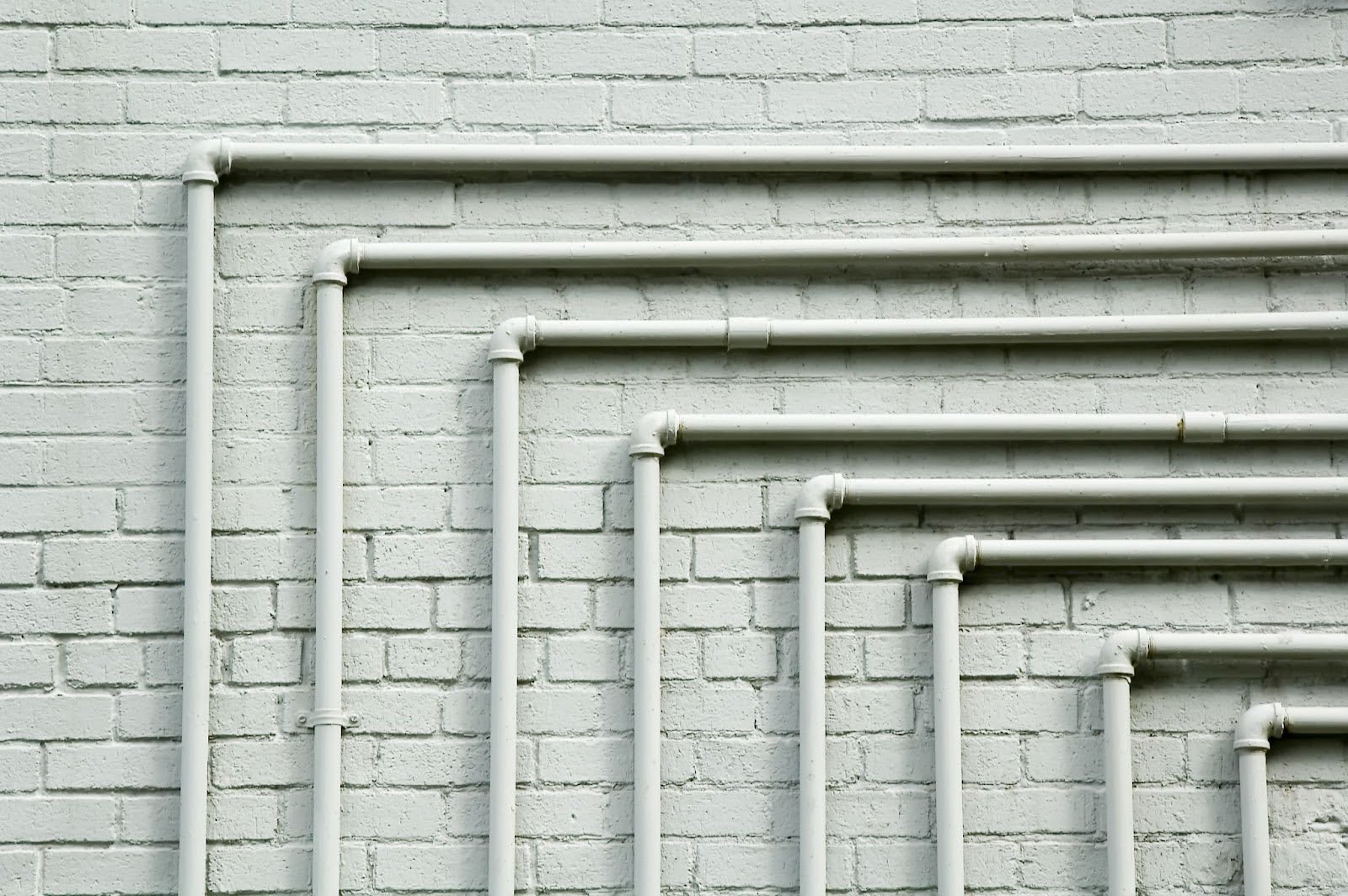 Parallel drain pipes featuring 90-degree turns mounted against a whitewashed brick wall.