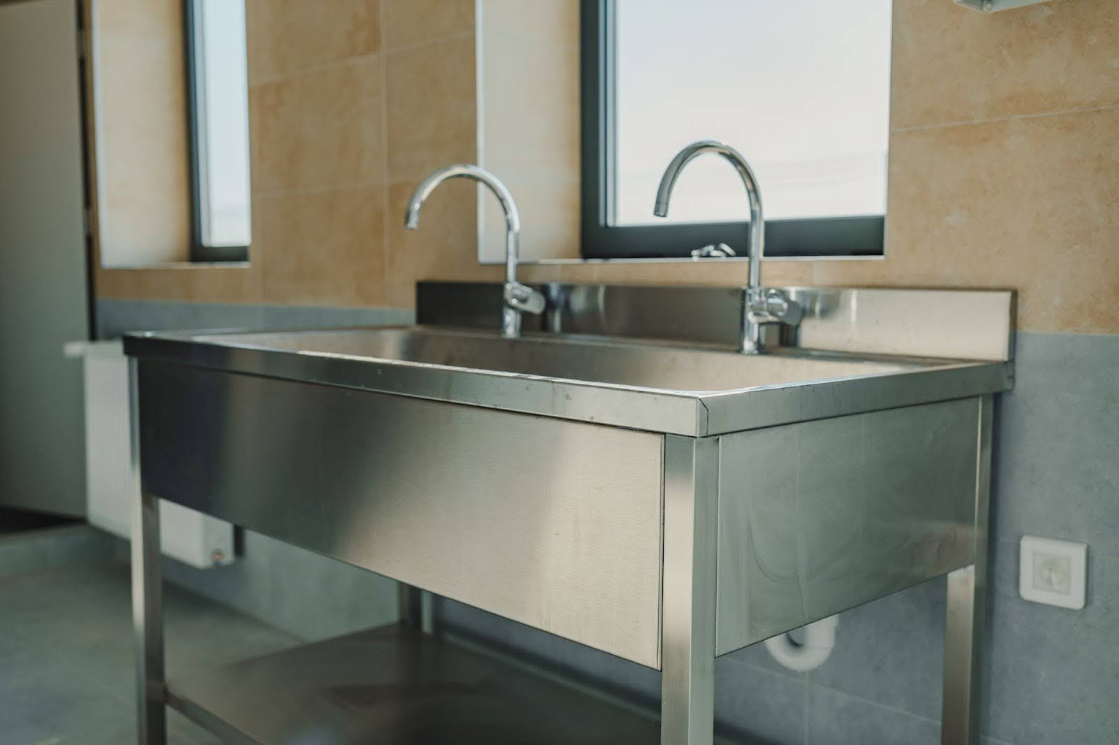 Commercial sink in a kitchen with a window in the background.
