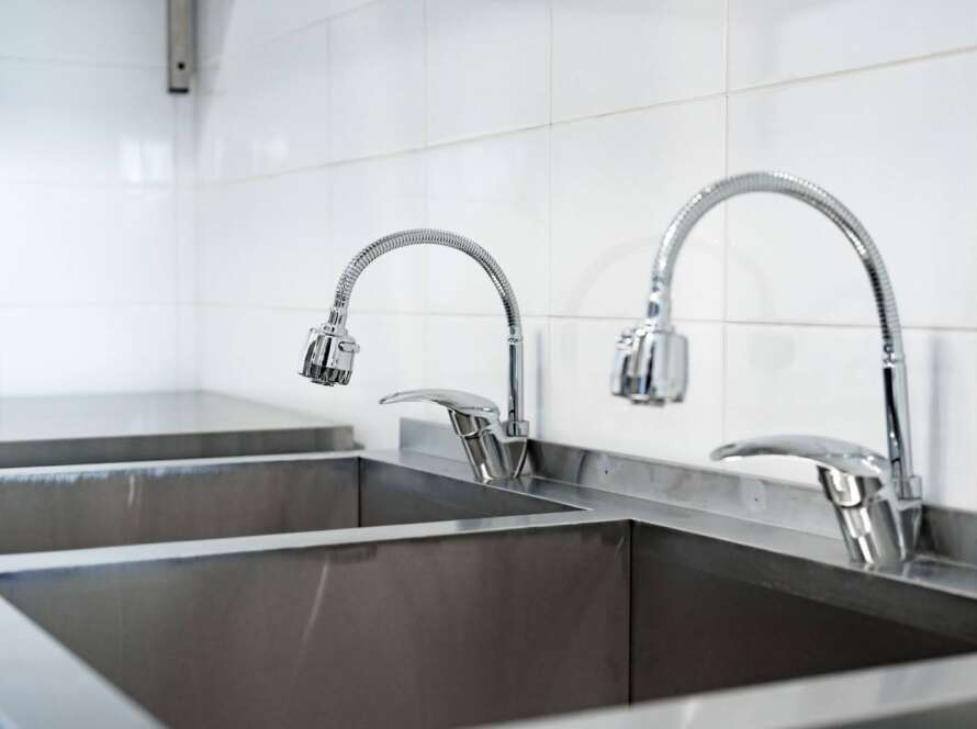 Two sink heads next to sinks in a commercial kitchen.