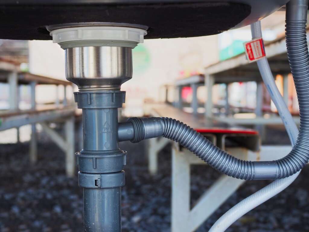 Metal sink siphon connected to a commercial garbage disposal drain line.