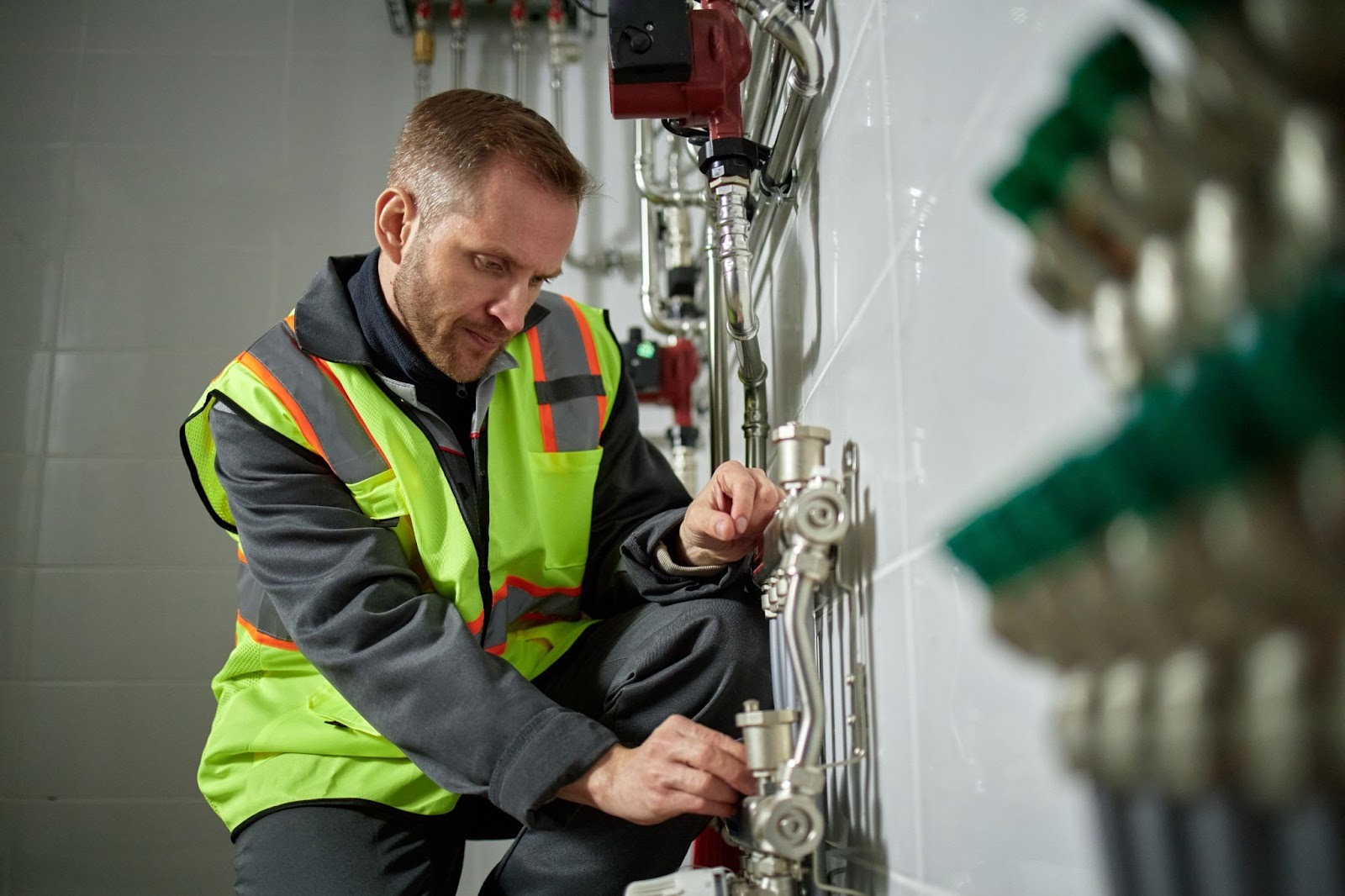 Caucasian commercial plumber inspecting and adjusting pipes in a building utility room