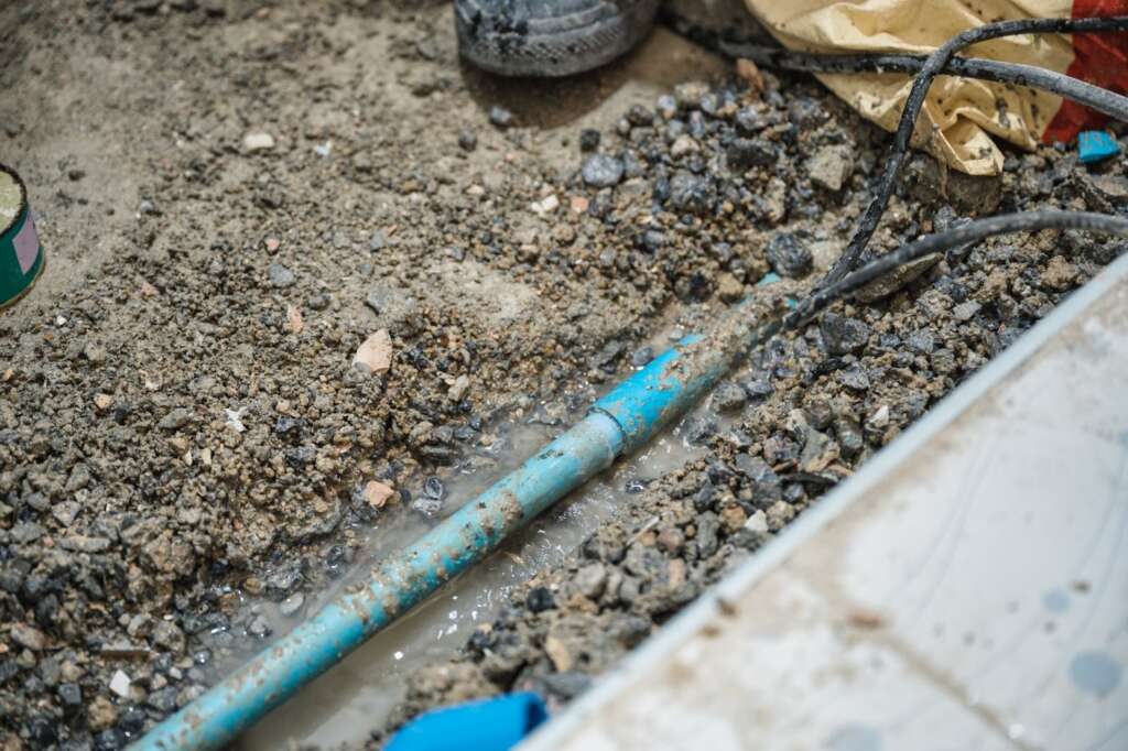 Bathroom demolition showing workers repairing a leaking sewer pipe beneath the floor.
