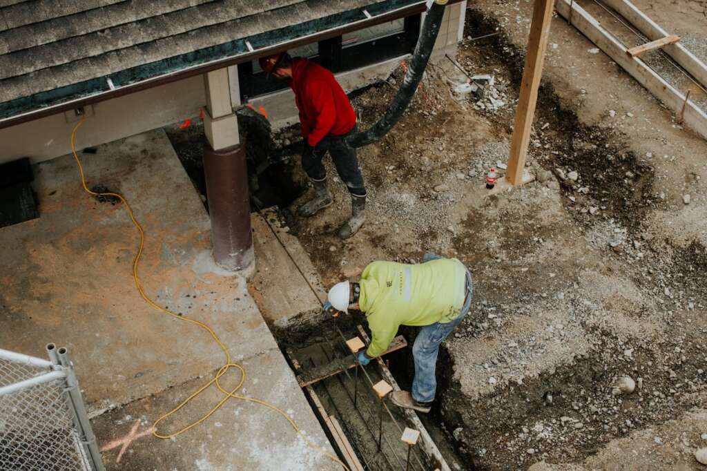 Plumbing professionals working on sump pump installation at a home construction site.